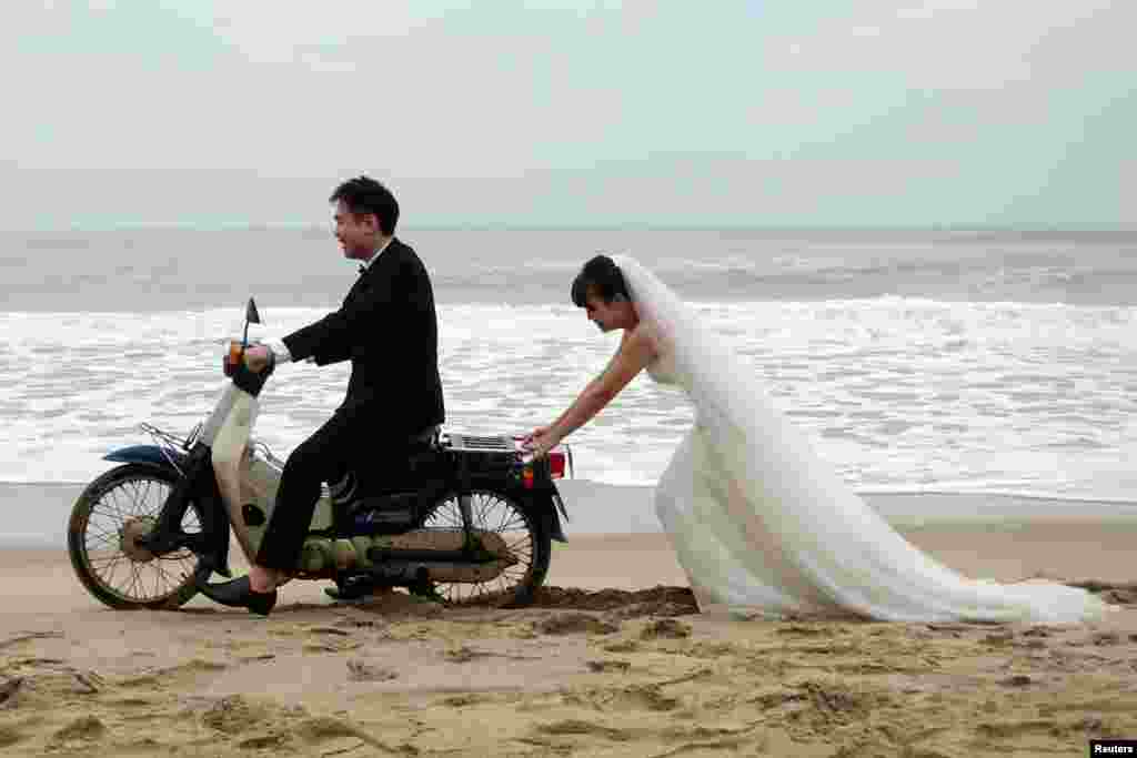 A Vietnamese bride is seen pushing the groom on a scooter during a photo shoot for their wedding in An Bang Beach outside Hoi An.