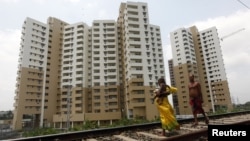 A woman carrying a child walks ahead of her husband on a railway track in front of residential buildings under construction on the outskirts of Kolkata, India, April 26, 2012.