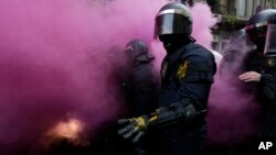 Catalan Mossos d'Esquadra regional police officers stand amid smoke from a smoke bomb during clashes with pro-independence supporters trying to reach the Spanish government office in Barcelona, Spain, Sunday, March 25, 2018. 