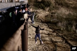 FILE - A migrant jumps the border fence to get into the U.S. side to San Diego, Calif., from Tijuana, Mexico, Jan. 1, 2019.