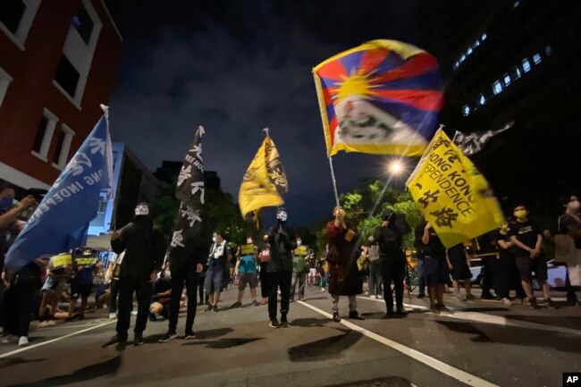 FILE - Hong Kong students in masks and other human rights activists chant and wave flags including the Tibetan flag outside the parliament building in Taipei, Taiwan, Oct 1, 2021.