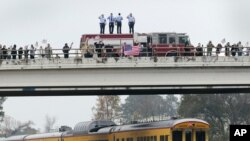 En un paso elevado, los bomberos saludan, junto con otros asistentes, el tren que lleva el cuerpo del expresidente George H.W. Bush.