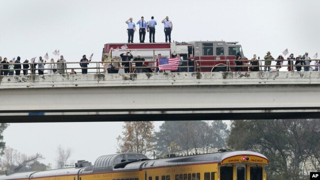 En un paso elevado, los bomberos saludan, junto con otros asistes, al tren que lleva el cuerpo del ex presidente George H.W. Bush.