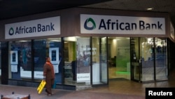 FILE - A cleaner walks past a branch of African Bank in Cape Town.