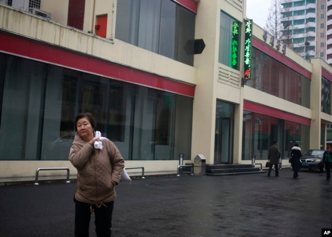 FILE - In this Dec. 21, 2018, photo, a North Korean woman walks outside Bugsae Shop, also known as the "Singapore Shop," in Pyongyang. Business is booming at such shops, which sell everything from Ukrainian vodka to brand-name knock-offs from China. The stores stock many of the very things U.N. sanctions banning trade in luxury goods are intended to block.