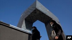 In this Thursday, Dec. 22, 2016 file photo, residents wearing masks walk in front of the iconic headquarters of China's state broadcaster Central China Television after a cold front pushed out heavy pollution from Beijing, China.
