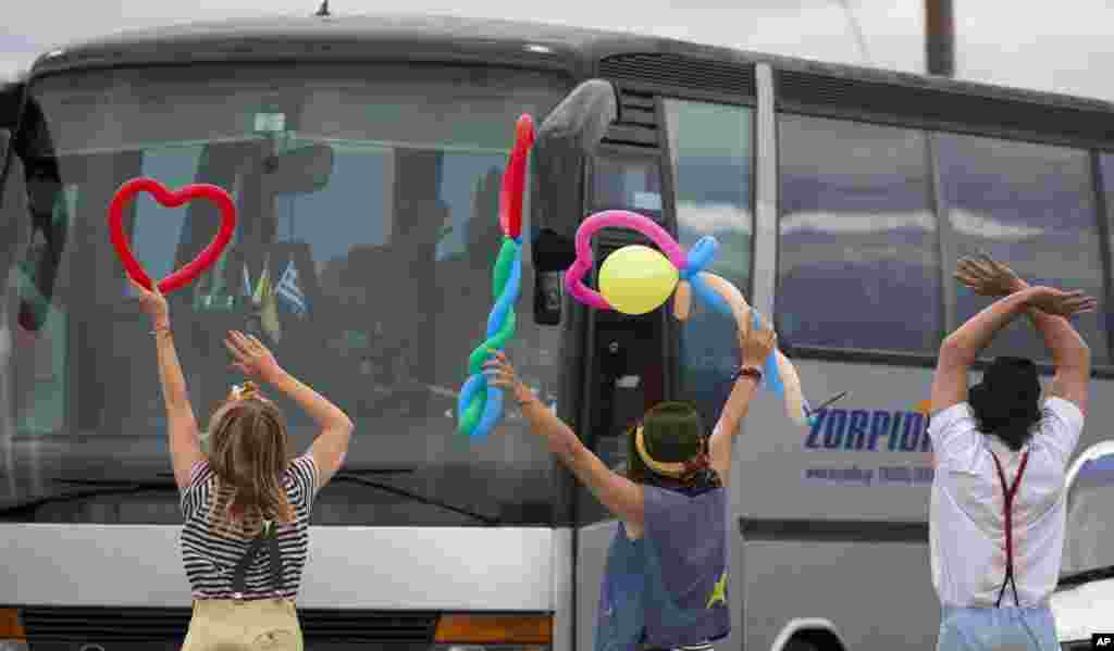 어린이들과 놀아주는 인도주의 활동가들이 그리스 이도메니 난민촌에서 이송되는 난민 버스를 향해 인사하고 있다. &nbsp;