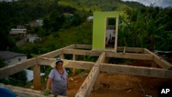 FILE - A woman poses for a portrait between the beams of her home being rebuilt after it was destroyed by Hurricane Maria one year ago in the San Lorenzo neighborhood of Morovis, Puerto Rico, Sept. 8, 2018.