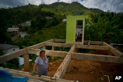 FILE - A woman is pictured between the beams of her home being rebuilt after it was destroyed by Hurricane Maria a year earlier in the San Lorenzo neighborhood of Morovis, Puerto Rico, Sept. 8, 2018.
