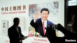 A man poses for pictures at a booth of China's President Xi Jinping books, translated in foreign languages, which are on display during the China International Import Expo at the National Exhibition and Convention Center in Shanghai, China, November 7, 20
