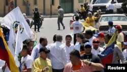 Un hombre encapuchado apunta con un arma a un grupo de personas que caminan con el líder opositor venezolano Juan Guaidó.