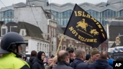 FILE - Riots police separate pro- and anti-immigration demonstrators as a man waves a flag reading "Islamists Not Welcome" during a demonstration in Amsterdam, Feb. 6, 2016. 