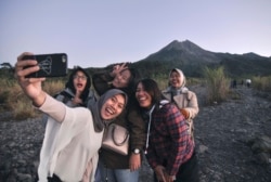 Wisatawan domestik berswafoto dengan latar belakang Gunung Merapi, Yogyakarta, 6 Agustus 2019. (Foto: AP)