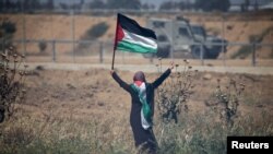 A woman holding a Palestinian flag gestures in front of Israeli forces during a protest marking the 71st anniversary of the 'Nakba', or catastrophe, at the Israel-Gaza border fence, in the southern Gaza Strip, May 15, 2019.