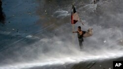 Archivo - Un manifestante ondea una bandera chilena mientras recibe el impacto de un cañon de agua, en Santiago, Chile, el 31 de octubre de 2019.