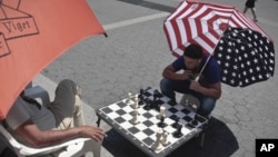 Estos dos neoyorquinos juegan ajedrez en la calle protegidos del ardiente sol por enormes sombrillas.