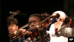 FILE: Migrant Miria, 8 from Angola, resident of the Karatepe municipality camp for refugees in the northeastern Greek island of Lesbos, that have been taught how to play the violin and sing, performs during a concert in Mytilene, Lesbos, Greece, Thursday, Dec. 15, 2016. (AP Photo/Lefteris Pitarakis)