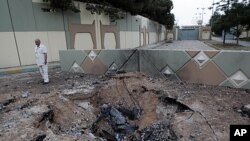 In this photo taken on a government organized tour a Libyan official stands next to a crater left after an airstrike at Moammar Gadhafi's Bab al-Aziziya compound in Tripoli, Libya, June 1, 2011.