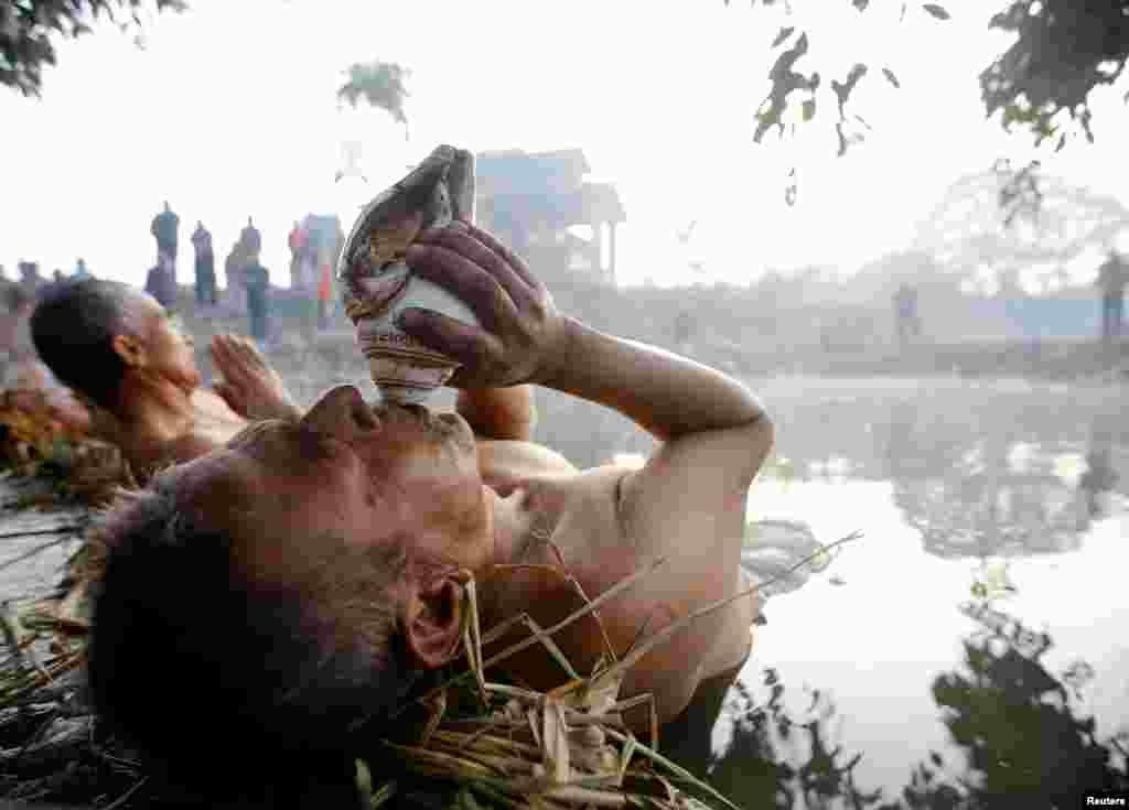 A devotee blows into a conch shell as he offers prayer by submerging in the Hanumante River during the Swasthani Brata Katha festival in Bhaktapur, Nepal.