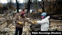 Vanthy Bizzle hands some small religious figurines to her husband Brett Bizzle in the remains of their home after returning for the first time since the start of the Camp Fire last November.