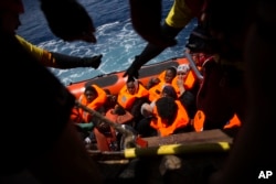 Women and children wait their turn to get on onboard the rescue vessel Golfo Azzurro by members of the Spanish NGO Proactiva Open Arms, after being rescued from a wooden boat sailing out of control in the Mediterranean Sea, about 18 miles north of Sabrath Libya, June 15, 2017.