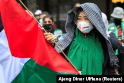 Seorang anggota organisasi buruh Indonesia memegang bendera Palestina saat melakukan aksi protes terhadap Israel di luar gedung PBB di Jakarta, 18 Mei 2021. (Foto: REUTERS/Ajeng Dinar Ulfiana)