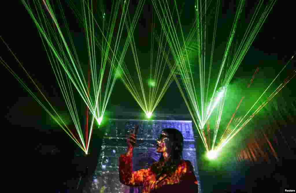 A visitor takes pictures with her mobile phone in front of laser beams and a projected image of the Arc de Triomphe, at the 2013 Optic Valley of China International Optoelectronic Exposition and Forum (OVC EXPO) in Wuhan, Hubei province, China. 
