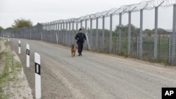 FILE - A police officer with a dog patrols the border fence on the Hungarian-Serbian border near Roszke, 180 kms southeast of Budapest, Hungary, April 28, 2017. Hungary has asked the EU to pay half of the cost of the fence built to keep illegal immigrants