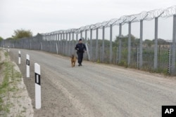 Un policía con un perro patrulla la valla fronteriza en la frontera húngara-serbia cerca de Roszke, a 180 km al sureste de Budapest, Hungría, el 28 de abril de 2017. Hungría ha pedido a la UE que pague la mitad del costo de la cerca construida para evitar el ingreso de inmigrants ilegales.