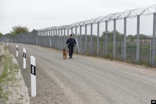 Un policía con un perro patrulla la valla fronteriza en la frontera húngara-serbia cerca de Roszke, a 180 km al sureste de Budapest, Hungría, el 28 de abril de 2017. Hungría ha pedido a la UE que pague la mitad del costo de la cerca construida para evitar el ingreso de inmigrants ilegales.