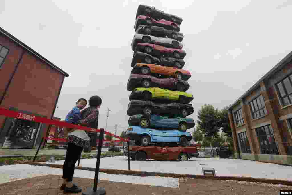 Ibu dan anaknya melihat hiasan kota yang terbuat dari 13 mobil bekas karya Gu Yuan dan Sun Yeli di sebuah taman industri budaya di Wuhan, provinsi Hubei, Cina.