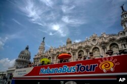 FILE - In this June 17, 2017, photo, tourists ride a tour bus in front of the Capitolio in Havana, Cuba.