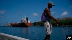 A fisherman walks on the Malecon seawall where an oil tanker can be see in the background in Havana, Cuba, April 17, 2019. Washington has sanctioned Venezuela’s oil industry and shipping companies that move Venezuelan oil to Cuba.