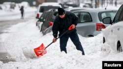 Un hombre palea para tratar de desatascar su vehículo que quedó atrapado por la nieve en Nueva York. 