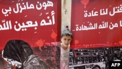 A child looks out from behind posters during a funeral ceremony in the Sayyida Zeinab mosque on the outskirts of Damascus on April 26, 2017, for the victims of a car bomb.