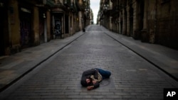 Seorang pria tidur di tengah jalan yang sepi di Barcelona, Spanyol, saat diberlakukannya karantina wilayah tersebut, 17 April 2020. (Foto: dok).