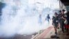 Reporters stand to the side of an anti-government protest as demonstrators standoff with police who fired tear gas, Bangkok, Thailand, Aug. 7 2021.