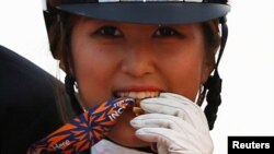 FILE - South Korea's Chung Yoo-ra, then known as Chung Yoo-yeon, bites her gold medal as she poses after winning the equestrian Dressage Team competition at the Dream Park Equestrian Venue during the 17th Asian Games in Incheon, Sept. 20, 2014.
