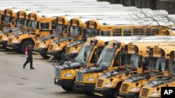 FILE - In this April 27, 2020, file photo, a worker passes public school buses parked at a depot in Manchester, N.H. (AP Photo/Charles Krupa, File)