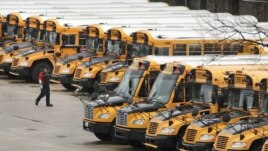 FILE - In this April 27, 2020, file photo, a worker passes public school buses parked at a depot in Manchester, N.H. (AP Photo/Charles Krupa, File)