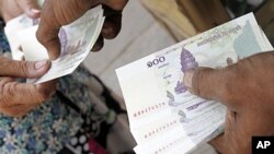 A man working at a money exchange (R) passes 100 Cambodian riel notes to a client in central Phnom Penh, file photo. 