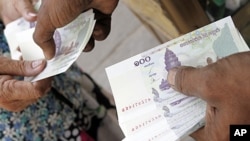 A man working at a money exchange (R) passes 100 Cambodian riel notes to a client in central Phnom Penh, file photo. 