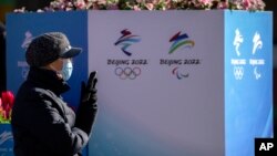 在北京的一條步行商業街上，一名戴著口罩的婦女坐在裝飾有北京冬奧會和殘奧會標誌的景觀附近。(2022年1月15日）