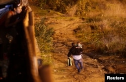 A migrant from Honduras, part of a caravan of thousands from Central America trying to reach the US, runs with his son after crossing illegally from Mexico by jumping a border fence, as they are photographed through the border wall in Tijuana, Mexico, Jan 13, 2019.