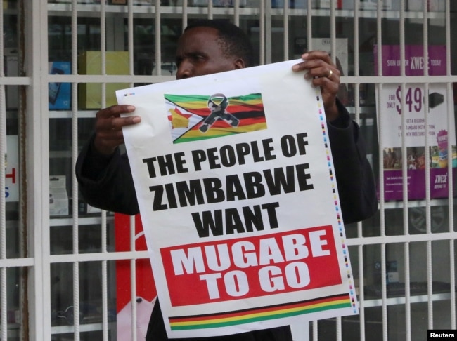 FILE - A man carries a poster calling for Zimbabwe President Robert Mugabe to step down as Zimbabweans take to the streets in Harare, Zimbabwe, Nov. 18, 2017.