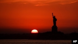 In this July 1, 2018 file photo, the sun sets behind the Statue of Liberty in New York. (AP Photo/Andres Kudacki, File)