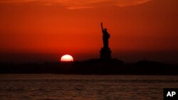 In this July 1, 2018 file photo, the sun sets behind the Statue of Liberty in New York as record high temperatures were recorded over the week in the U.S. and elsewhere. (AP Photo/Andres Kudacki, File)