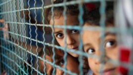 Palestinian children, who fled their homes due to Israeli air and artillery strikes, look through a window fence at a United Nations-run school where they take refuge, in Gaza City.