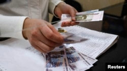 صندوق دار يک اداره پست در سیم فروپل (کريمه) در حال شمارش پرداخت حقوق بازنشستگی به روبل روسیه – ۵ فروردين ماه ( ۲۵ مارس ۲۰۱۴)