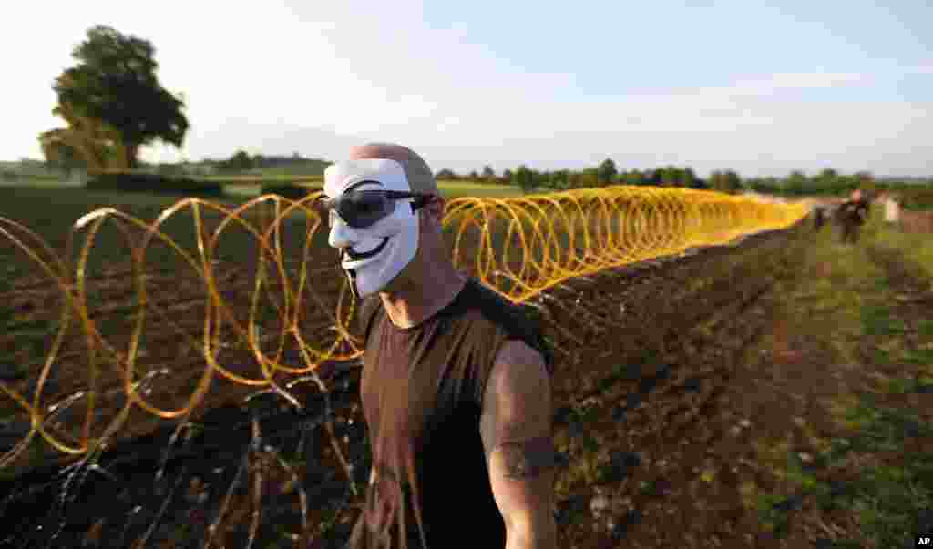 A protester in a Guy Fawkes mask walks past razor wire outside a security perimeter of the G8 summit in Enniskillen, Northern Ireland, June 17, 2013. 